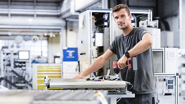 HR_young man works in the production, holds a drill in his hands