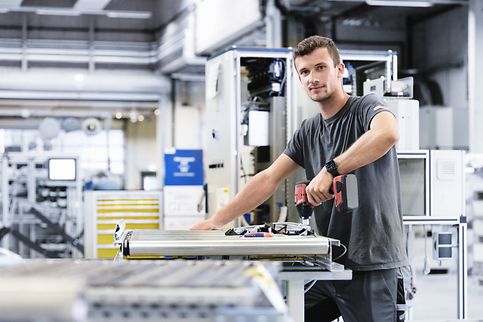 HR_młody mężczyzna pracuje na produkcji, trzyma w rękach wiertarkę