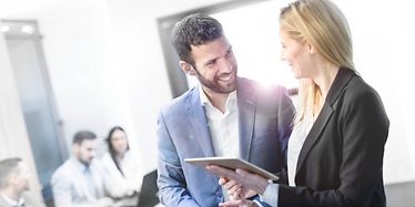 Man and woman are discussing in an office with people sitting on a desk