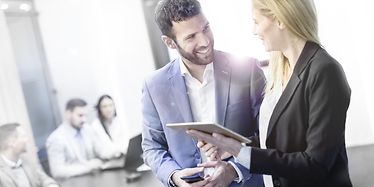 Man and woman are discussing in an office with people sitting on a desk